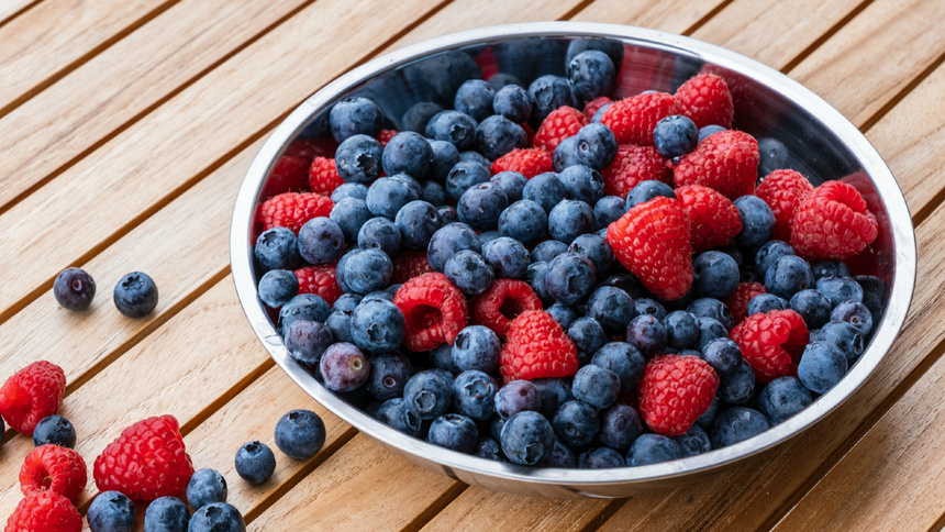 Eine silberne Schüssel mit Blaubeeren und Himbeeren steht auf einem Holztisch