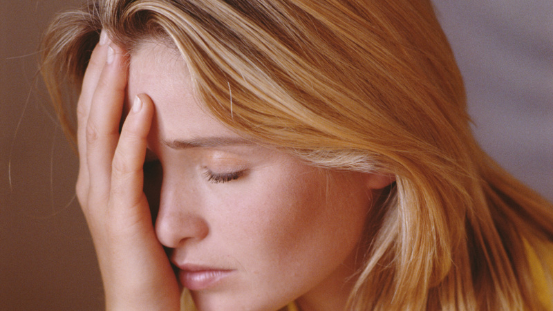 Une jeune femme se tient le front en fermant les yeux.