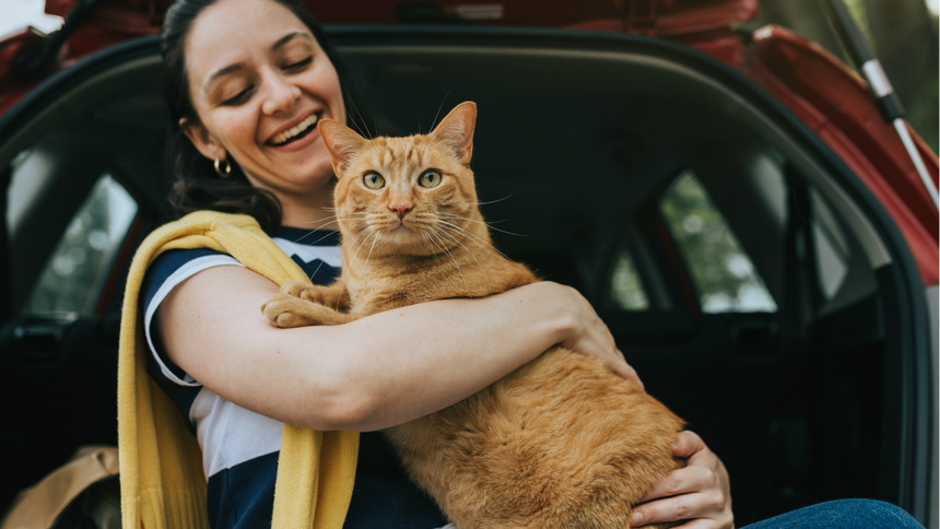 EIne Frau trägt lachend ihre Katze zum Auto