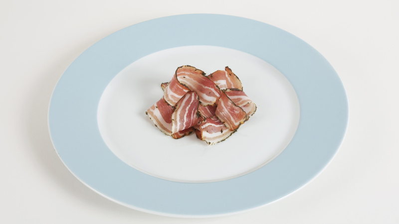 Une assiette blanche avec un bord bleu clair qui contient un petit tas de lard fumé.