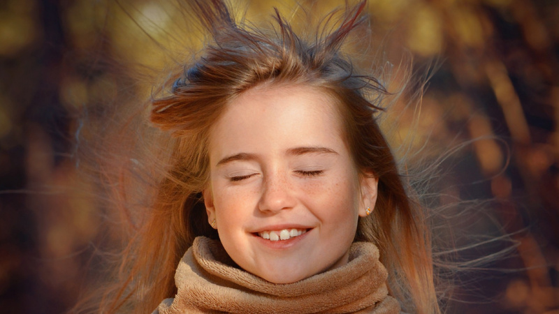 Ein Mädchen mit geschlossenen Augen. Der Wind bläst durch ihr Haar.