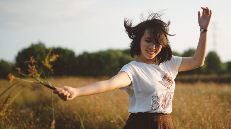 Cosmétique naturelle durabilité équitabilité: une femme s'amuse dans un pré. Elle tient un bouquet dans la main.