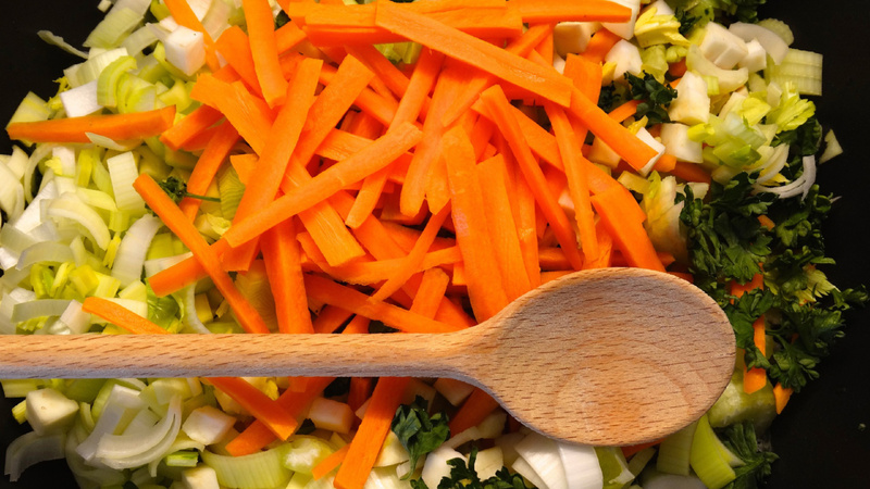 Alimentation substances vitales micronutriments cuisson: des poireaux, des carottes et du persil coupés en petits morceaux avec une cuillère en bois posée dessus.