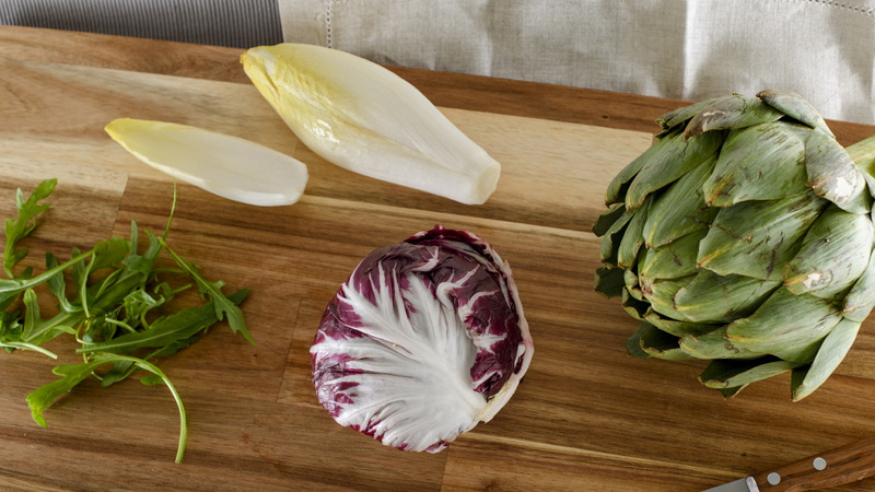 Verdauung, Darm, Magen-Darm: Holzschneidebrett, darauf liegen eine Artischocke, ein Chicorée, Rucola und ein Chicorino Rosso