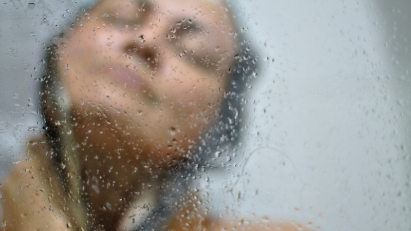 Intimpflege, Tabu, Beratung, Drogerie: Gesicht einer Frau hinter der Scheibe einer Dusche, darauf Wasserperlen