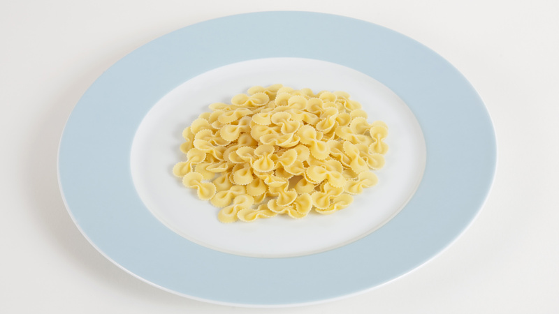 Une assiette blanche avec un bord bleu clair qui contient des pâtes.