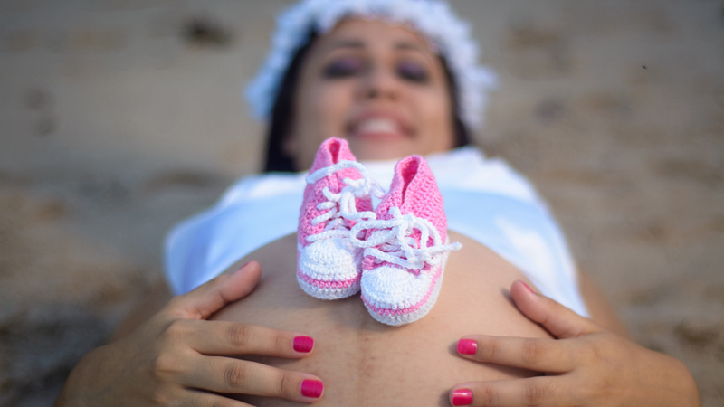 Schwangerschaft, Vitalstoffe, Mineralstoffe, Ernährung: Schwangere liegt auf dem Rücken, auf ihrem nackten Bauch ein paar rosa Babyschuhe