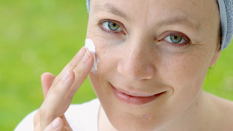 Cosmétique naturelle passage réussi: gros-plan sur le visage d'une femme qui se met de la crème sur la pommette droite.