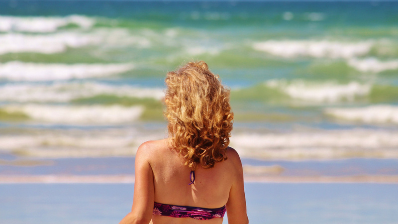 Schönheit, Pflege, Haut, Sommer: Frau im Bikini steht am Strand und schaut aufs Meer