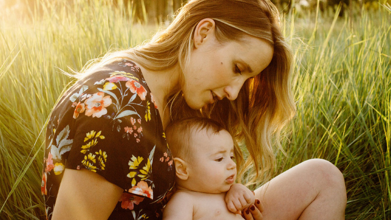 Une maman a un bébé entre les jambes. Ils sont habillés en été