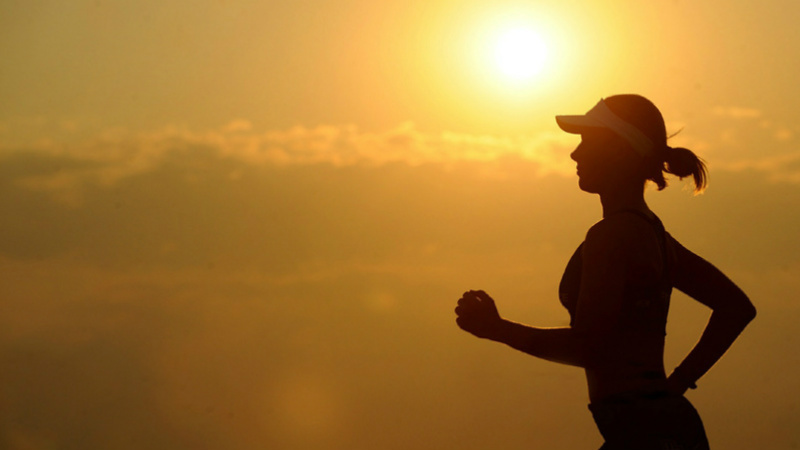 Une femme de profil court avec le soleil en arrière-plan