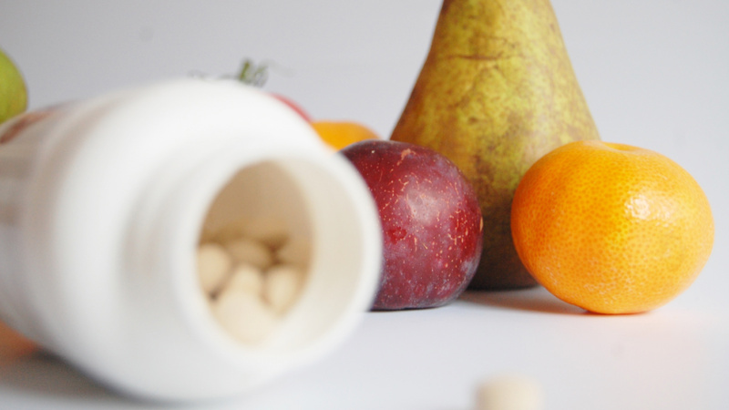 Alimentation substances vitales micronutriments hiver: une boîte de pilules renversée avec une poire, une prune et une mandarine en arrière-plan. 