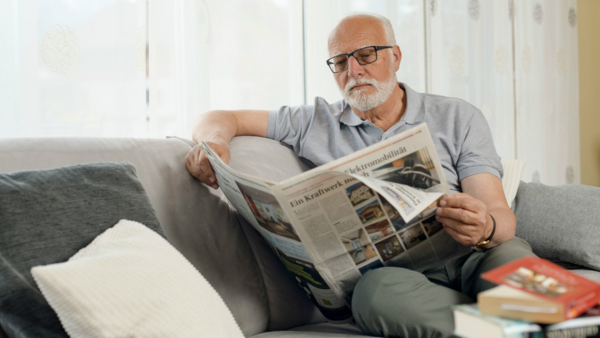 Alter, Gehirn, Demenz: Alter Mann sitzt auf einem Sofa und liest in einer Zeitung.