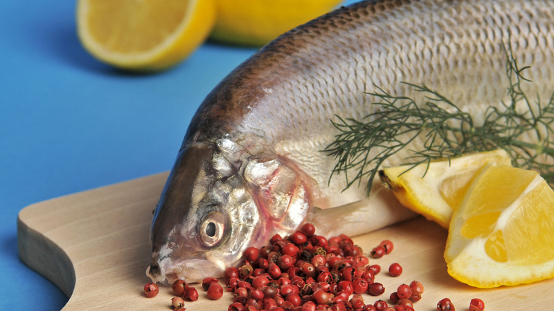 Alimentation graisses oméga sains: un poisson sur une planche en bois avec devant des grains de poivre et des quartiers de citron.