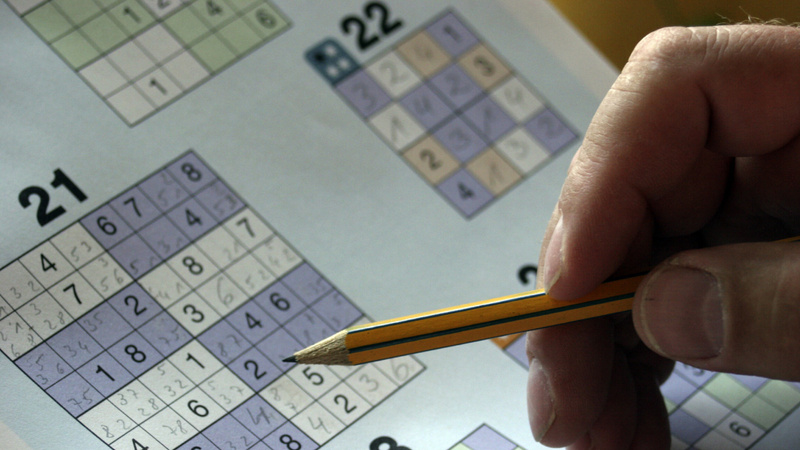 Psychologie, Konzentration, Gehirn, Gedächtnis: Hand hält einen Bleistift, im Hintrgrund ein Sudoku-Rätsel.