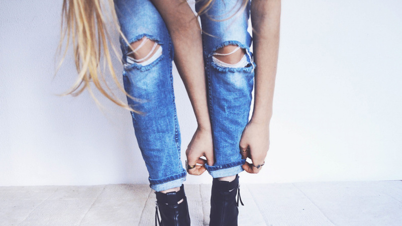 Les jambes d'une jeune fille qui porte un jean troué aux genoux et qui relève le bas de son canon gauche