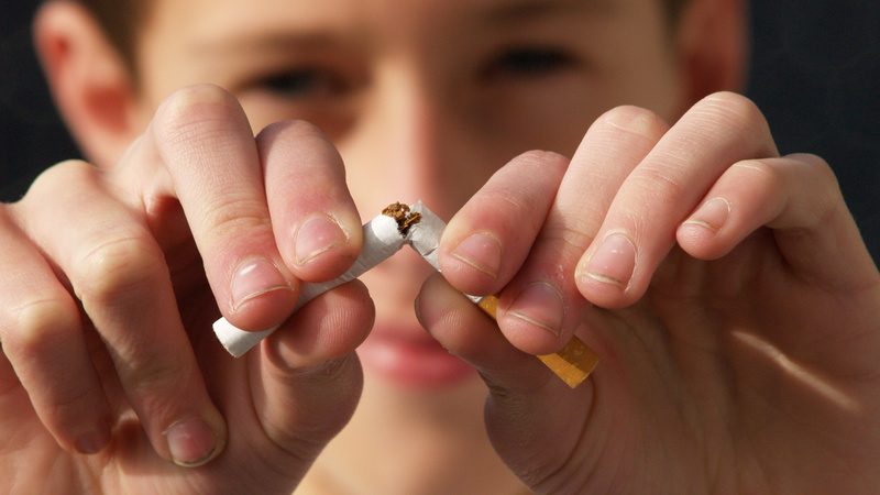 Rauchen, Rauchstopp, Nichtraucher: Gesicht eines jungen Mannes unscharf im Hintergrund, im Vordergrund seine beiden Hände. Er zerbricht eine Zigarette