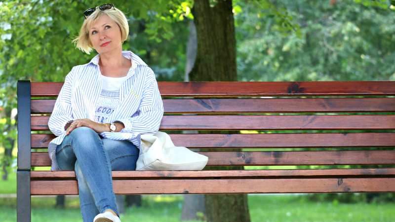 Frau mittleren Alters sitzt auf einer Parkbank