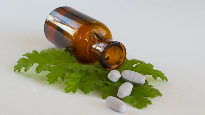 Une fiole brune en verre posée sur le côté sur une feuille verte des comprimés blancs sortent du flacon