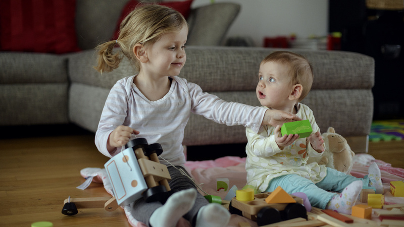 Un bébé est assis par terre avec sa grande sœur. Ils jouent ensemble.