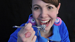 Une femme en pullover bleu tient une fourchette de trombones en métal qu'elle s'apprête à manger.